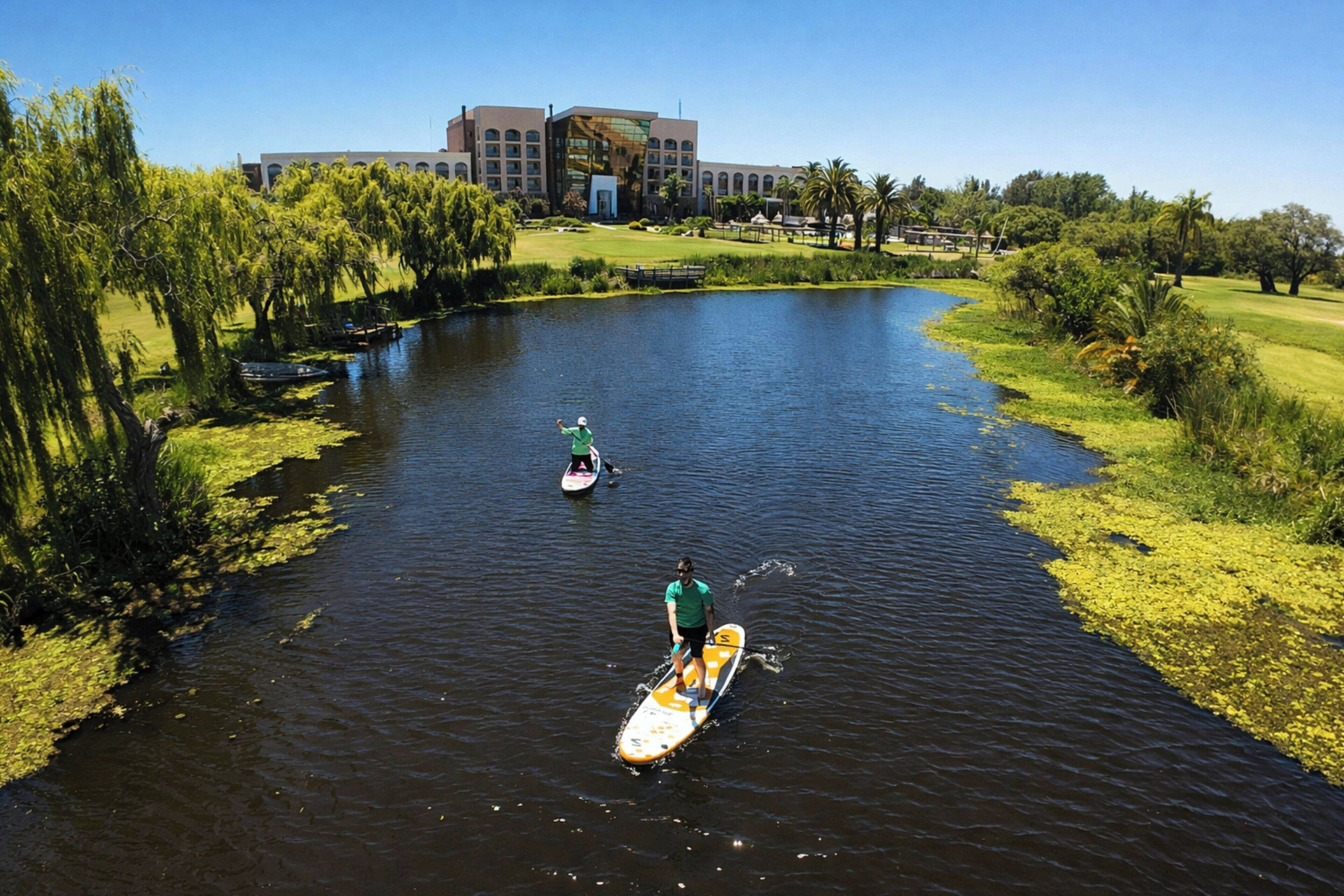 A river with paddleboards, a building in the background, and greenery along the banks.