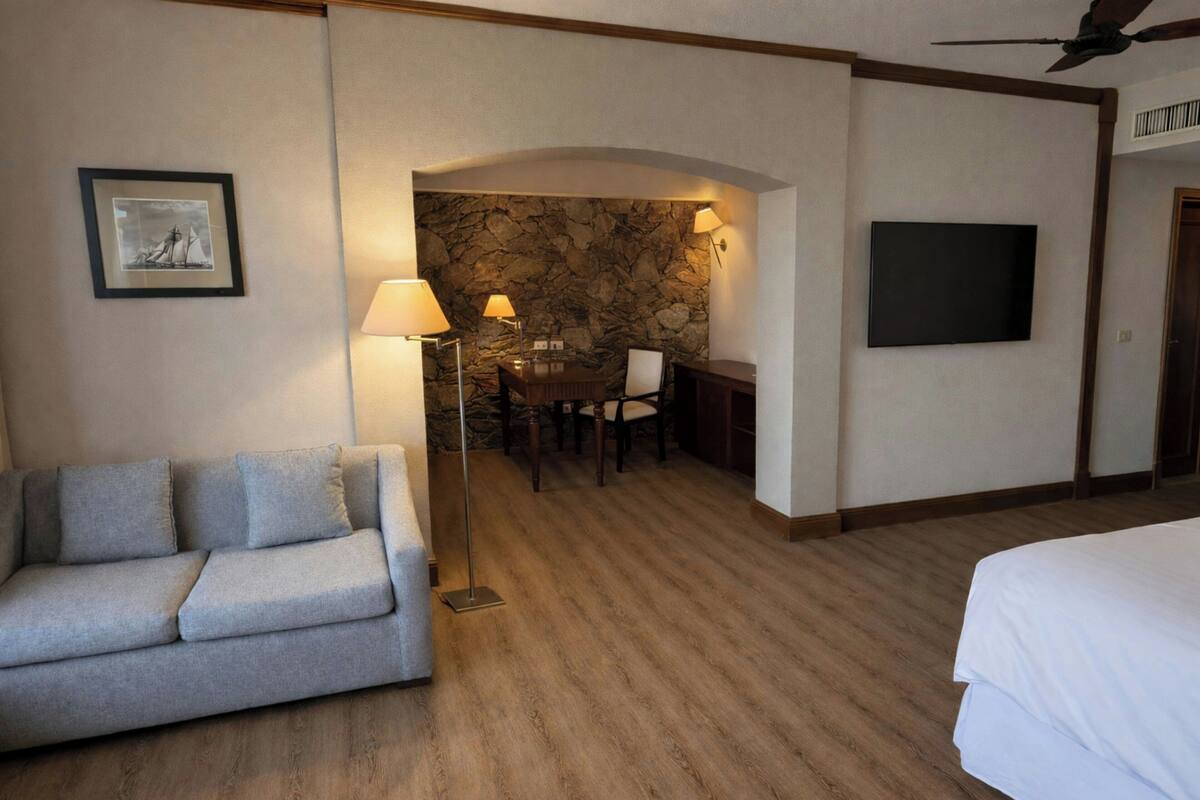 Habitación de hotel con sofá, mesa de comedor con sillas, televisor y una pared de piedra decorativa.