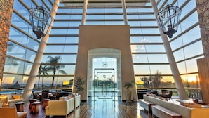 A spacious lobby with a high ceiling, large windows, and a view of the sunset.
