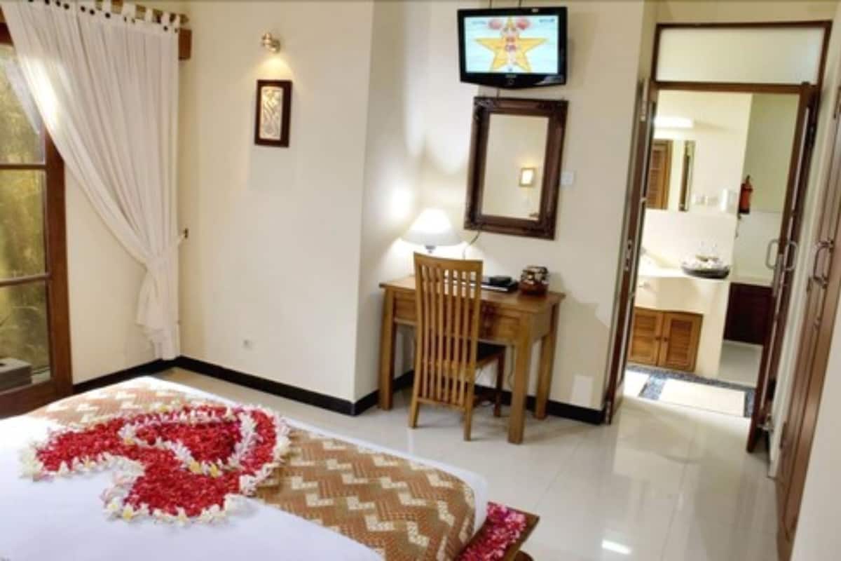 A hotel room with a bed, a desk, a chair, a television, and a bathroom visible through an open door.