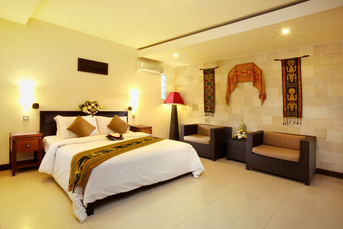 A hotel room with a large bed, a sofa, a nightstand, a lamp, and decorative wall hangings.