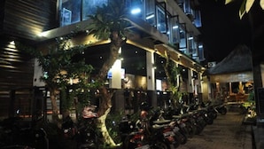 A modern building with a covered outdoor seating area, surrounded by trees and parked motorcycles. - Putu Bali Villa and Spa (Seminyak)