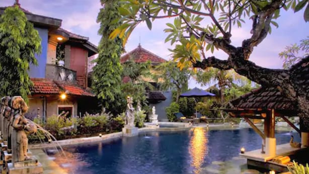 A serene pool area with a statue, a gazebo, and a traditional building with a tiled roof. - Putu Bali Villa and Spa (Seminyak)