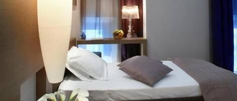 A modern hotel room with a bed, bedside table, lamp, and a vase with flowers.