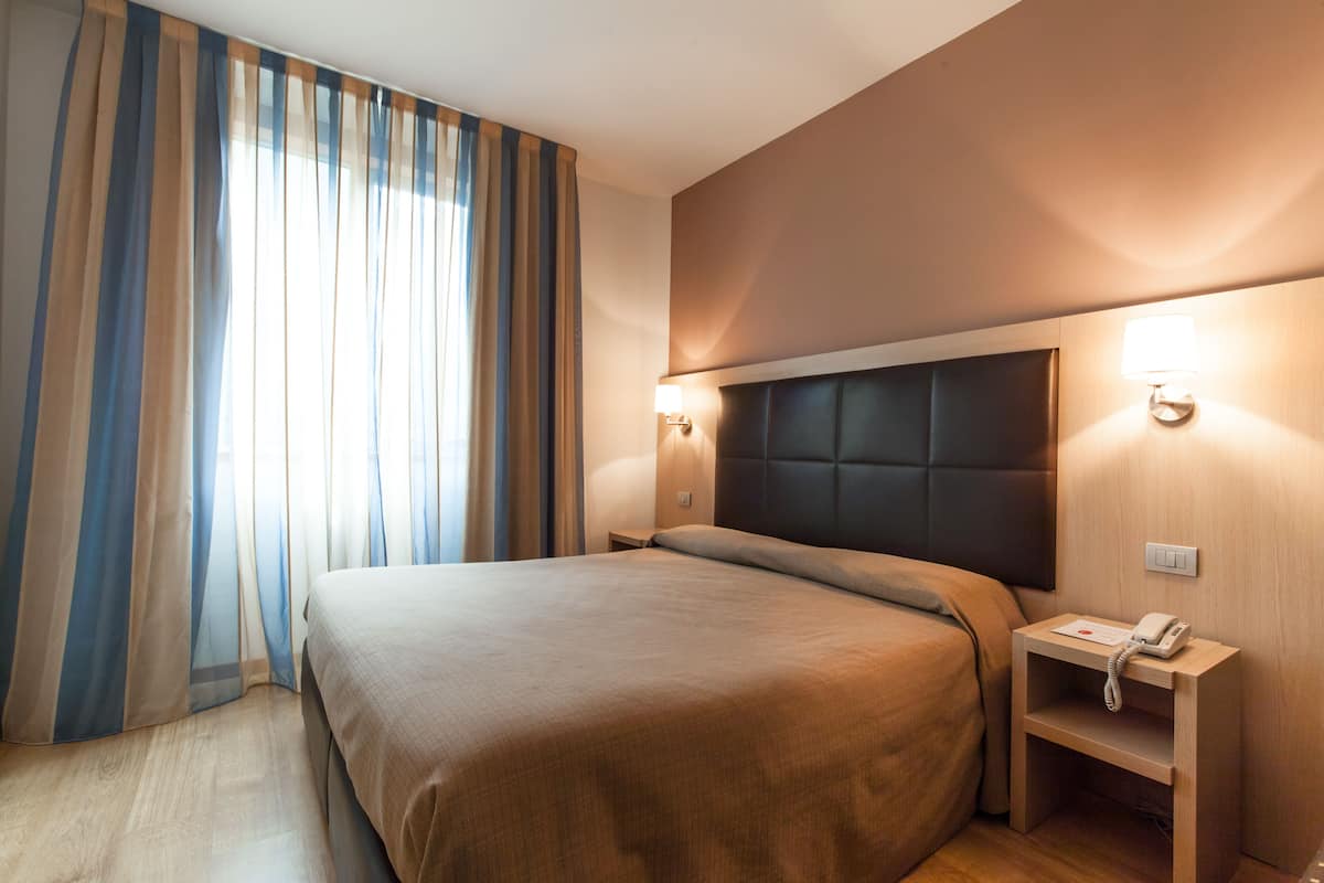 Una habitación de hotel con una cama grande, una mesita de noche con un teléfono y una lámpara de pared.