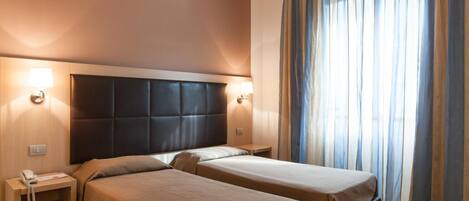 A hotel room with two beds, a headboard, bedside lamps, a telephone, and a window with curtains.