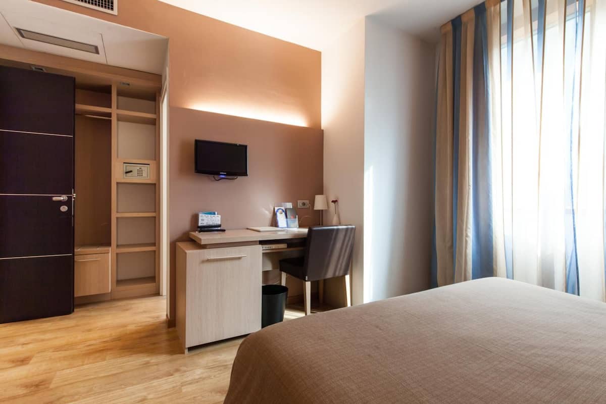 Habitación de hotel con cama, escritorio, silla, televisor y armario.