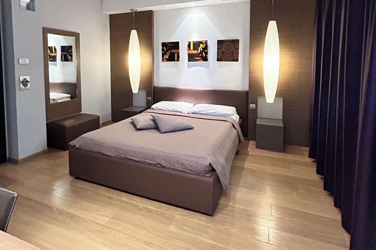 Una habitación de hotel moderna con una cama grande, mesitas de noche, un espejo y obras de arte en las paredes.