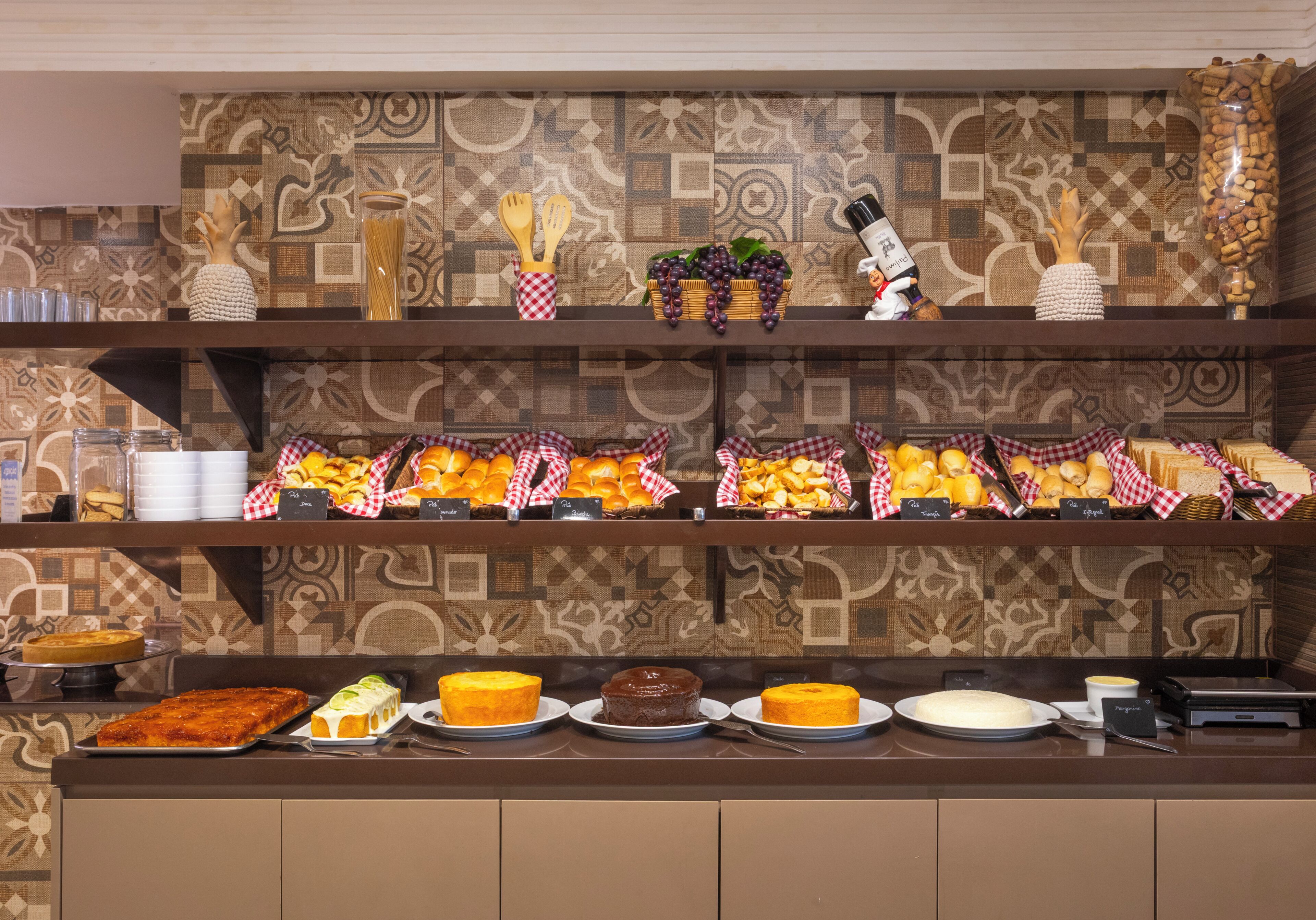 A buffet with various food items, including cakes and fruits, arranged on a counter with a patterned wall in the background.