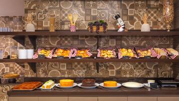 A buffet with various food items, including cakes and fruits, arranged on a counter with a patterned wall in the background.