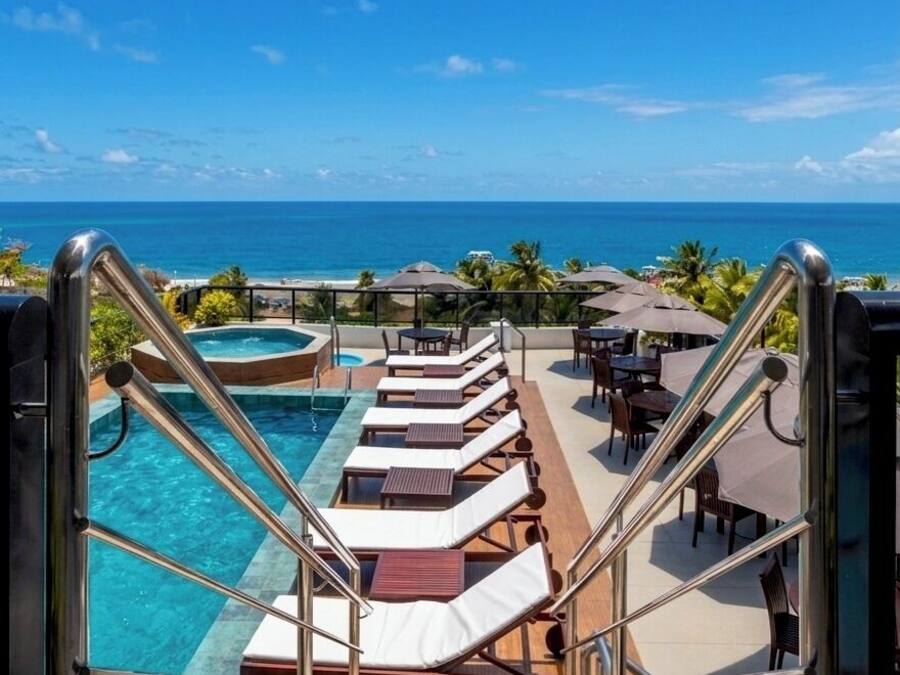 A poolside area with lounge chairs, a hot tub, and a view of the ocean.