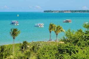 Vista sulla costa con barche sull'acqua, palme e una linea di costa distante con edifici.