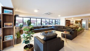 A modern living room with a sectional sofa, a coffee table, and a bookshelf with framed pictures. - Atlântico Praia Hotel (João Pessoa)