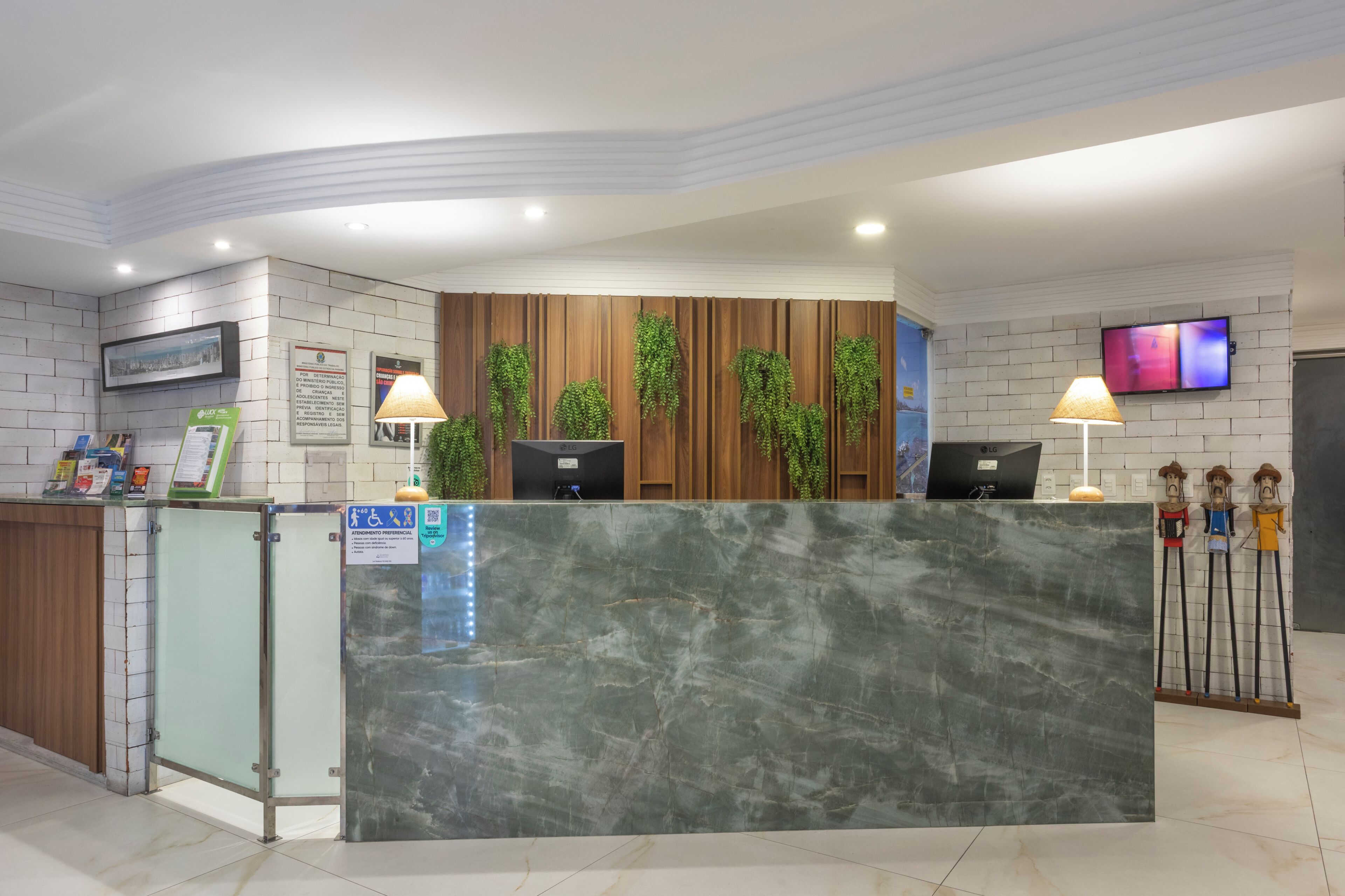 Balcão de recepção de hotel com bancada de mármore, painel de parede em madeira e televisão fixada na parede.