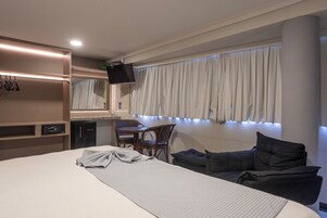 A hotel room with a bed, a desk with a chair, a television, and a window with curtains.