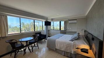 A hotel room with a bed, a desk, a chair, a small table, and a TV.