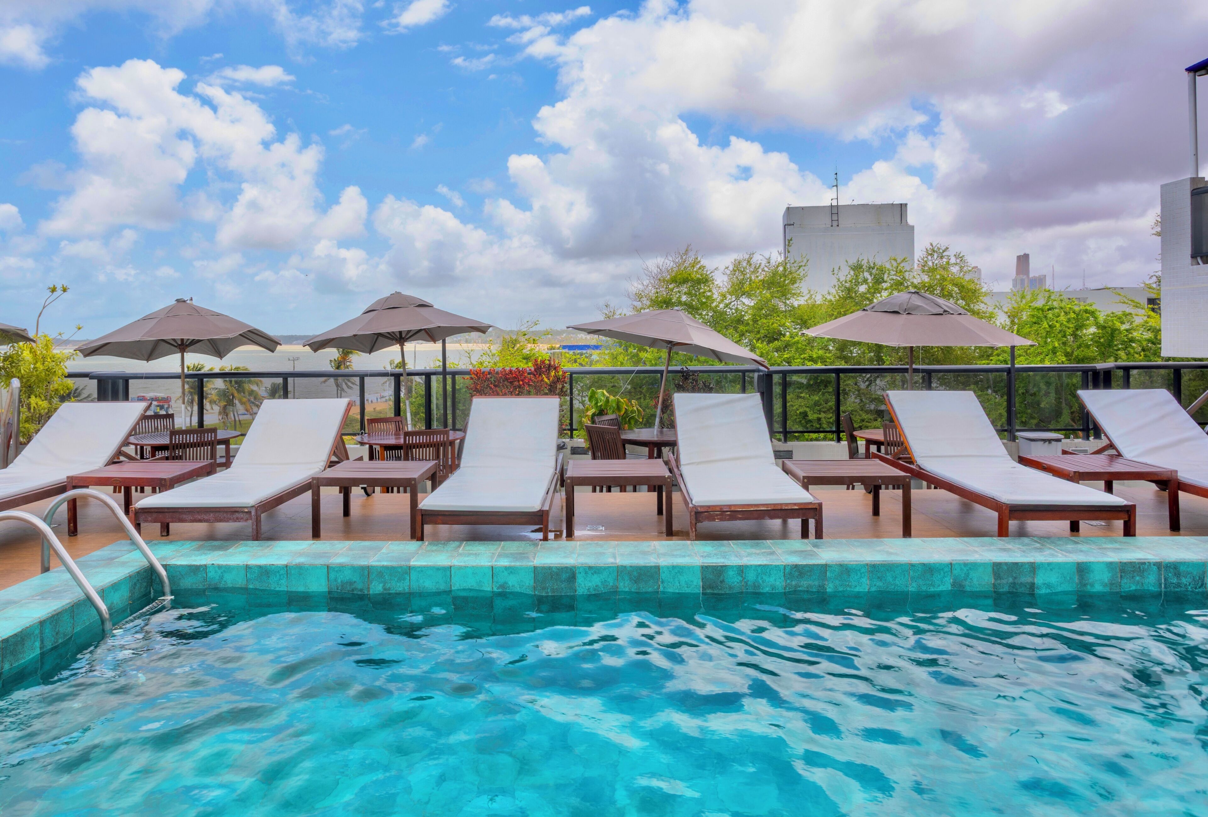 A poolside area with lounge chairs and umbrellas, a clear sky, and a view of buildings in the background.