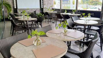 A restaurant with round tables and wicker chairs, a projector screen, and a view of the outside.