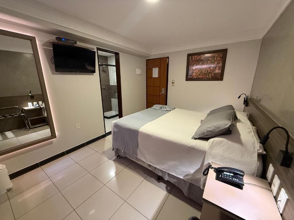 A hotel room with a bed, a TV, a painting, and a desk with a phone.
