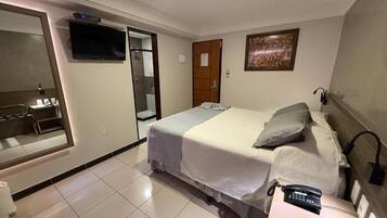 A hotel room with a bed, a TV, a painting, and a desk with a phone.