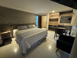 Una moderna camera d'albergo con un letto grande, comodini, una scrivania con una sedia, uno specchio e un bagno visibile attraverso una porta aperta.