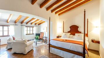 Un dormitorio amplio con cama con dosel, una sala de estar con sofá y sillones, y vistas al exterior a través de grandes ventanales.