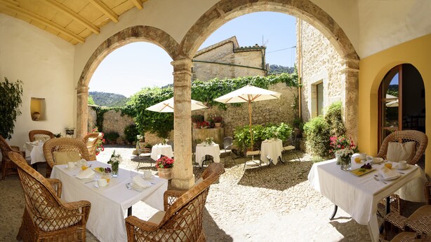 An outdoor dining area with tables and chairs, surrounded by stone walls and arches, featuring potted plants and umbrellas. - Finca Son Palou (Bunyola)