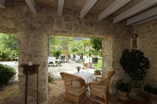 An outdoor patio area with stone walls, wicker furniture, and a view of a landscaped garden. - Finca Son Palou (Bunyola)