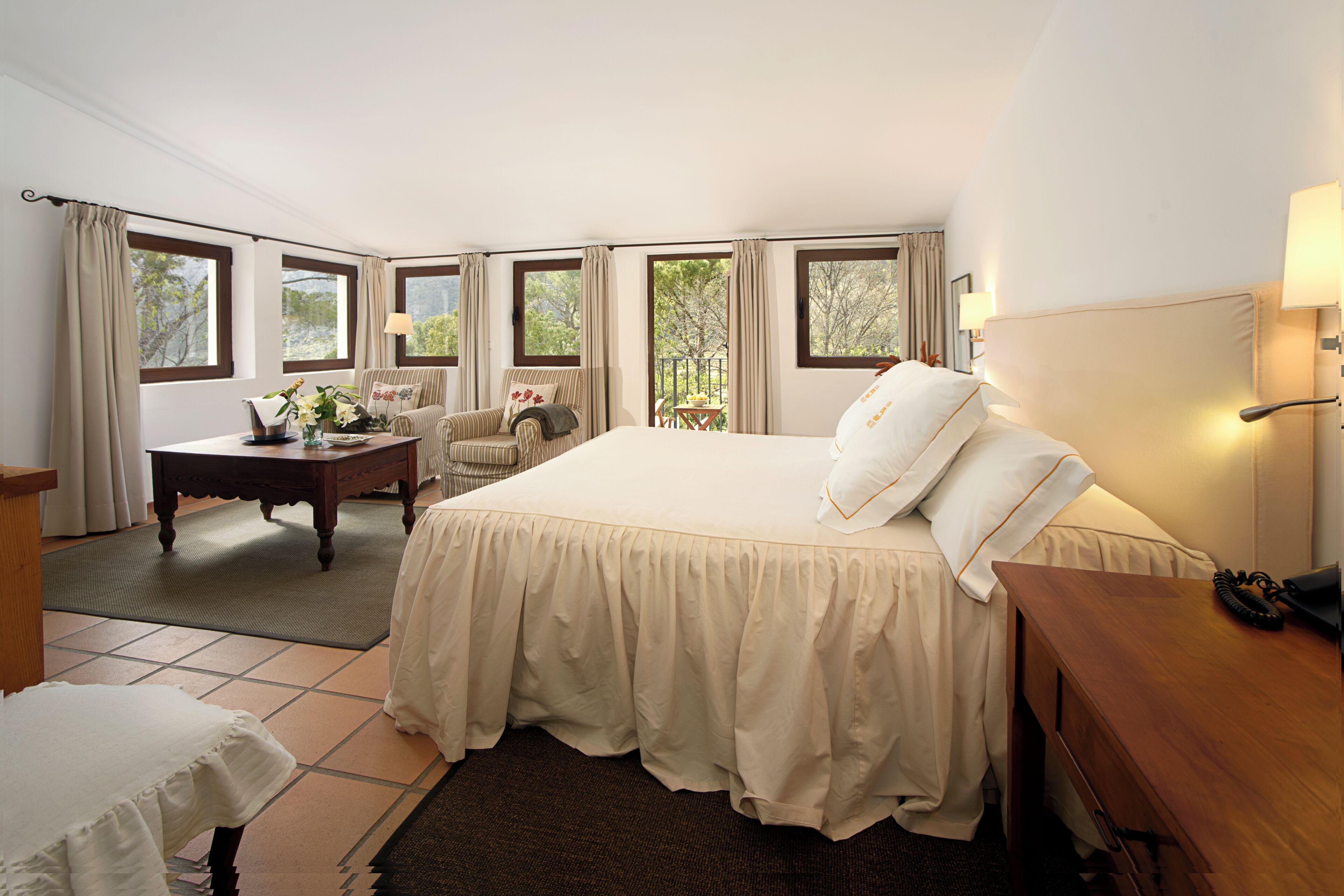 Habitación de hotel con una cama grande, un escritorio, una silla y vistas al exterior a través de amplias ventanas.