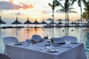 Une table dressée pour un repas, avec vue sur des palmiers et un coucher de soleil sur l’eau.
