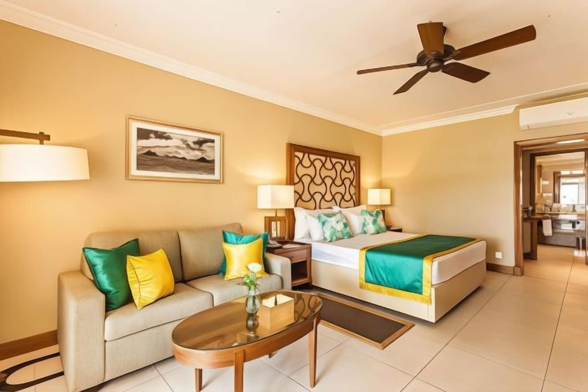 A hotel room with a bed, a sofa, a coffee table, and a ceiling fan.