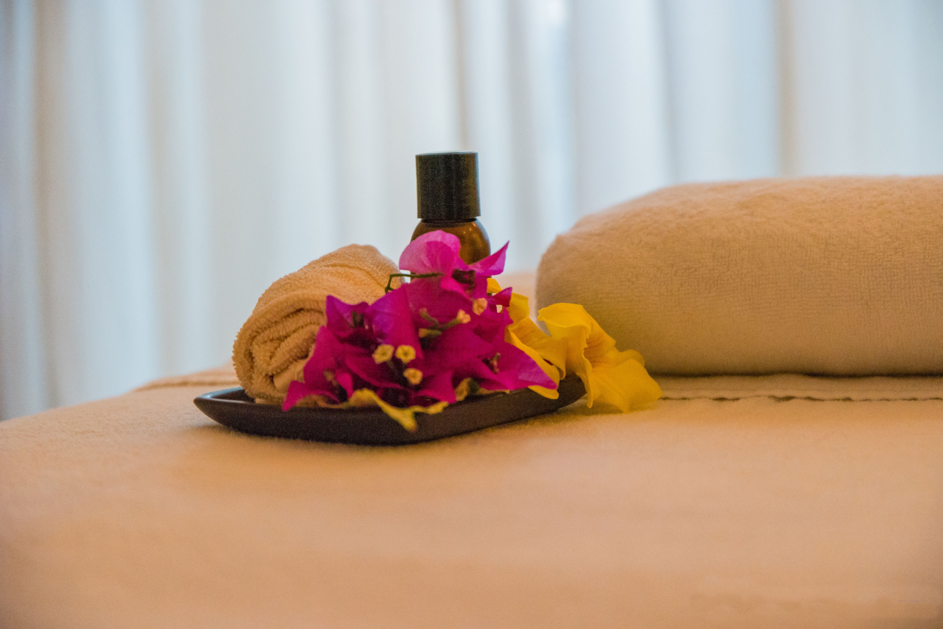 Un entorno de spa con una toalla, una botella de aceite esencial y flores de colores sobre una superficie acolchada.