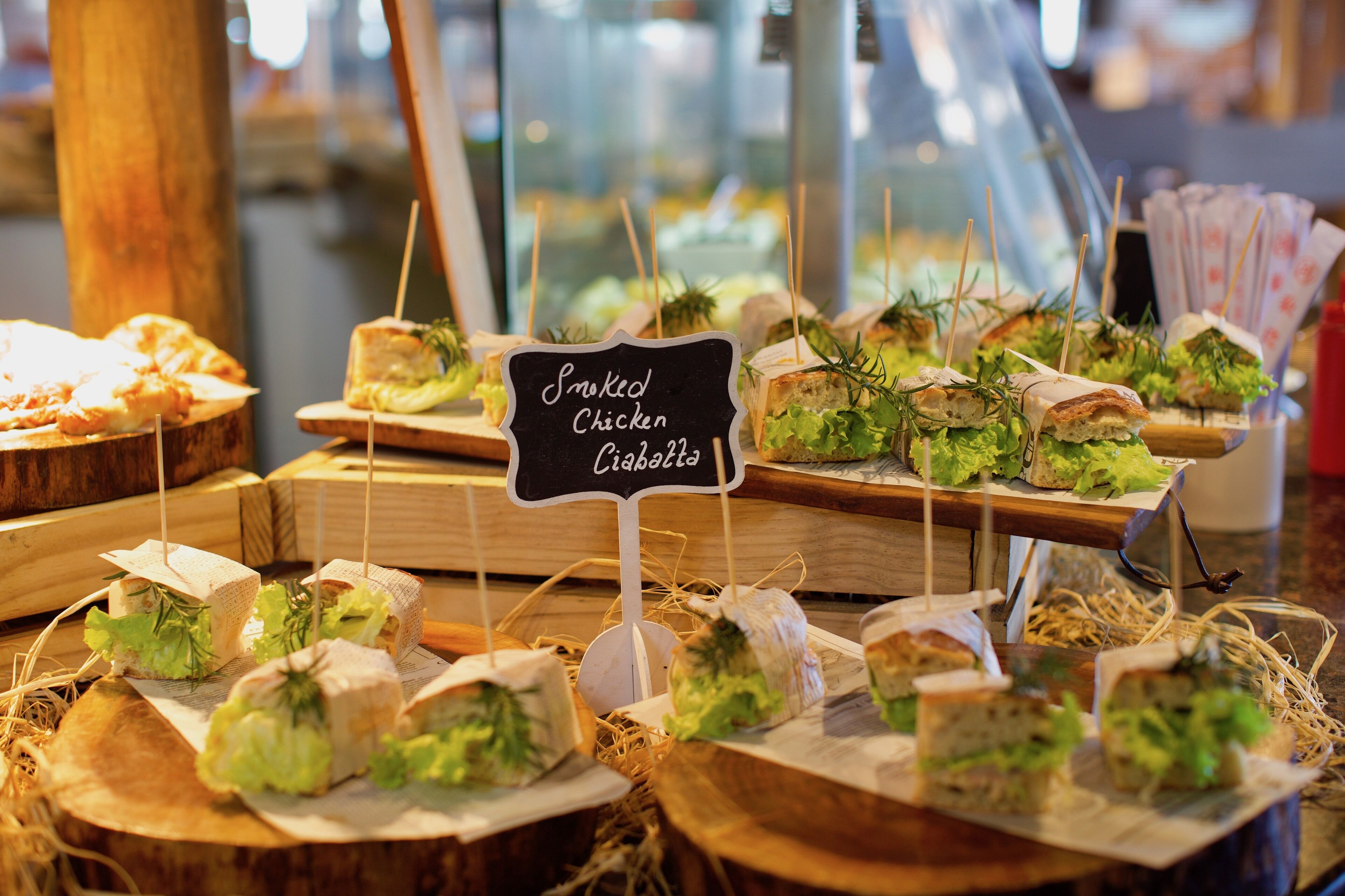 A display of smoked chicken ciabatta sandwiches with toothpicks, arranged on wooden boards.