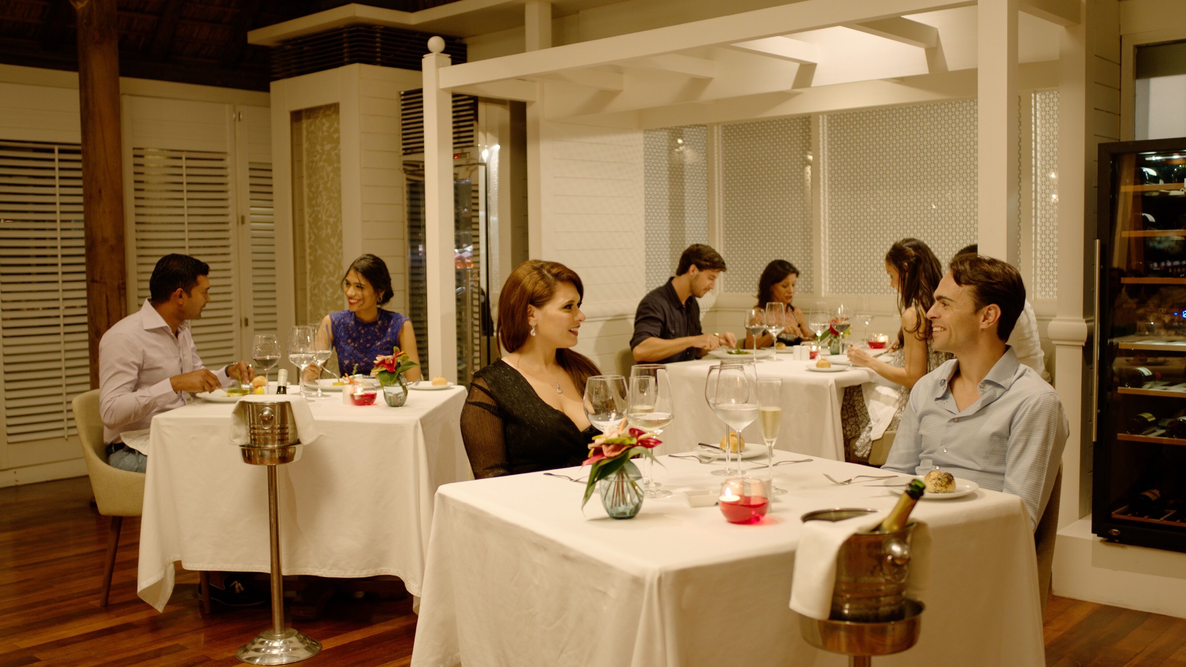A dining area with round tables, white tablecloths, and a wine rack.