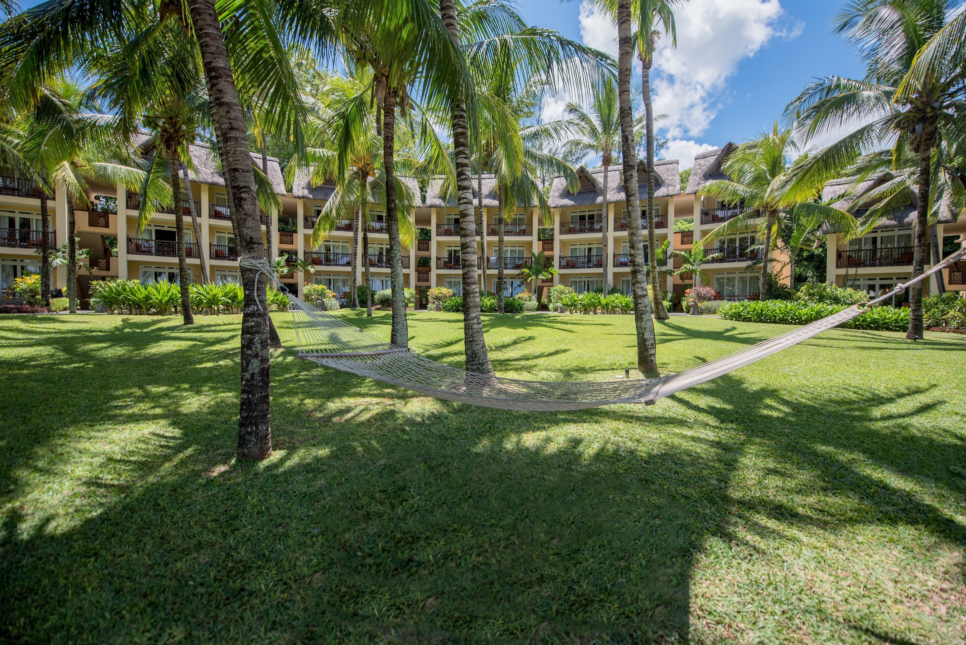 Un resort con edificios de varios pisos, palmeras y una hamaca en el patio.