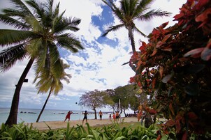 Partido de voleibol de playa con palmeras y el océano al fondo.