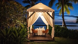Un belvédère abritant une table et des chaises, aménagé pour les repas, entouré d’une végétation luxuriante et offrant une vue sur une étendue d’eau.
