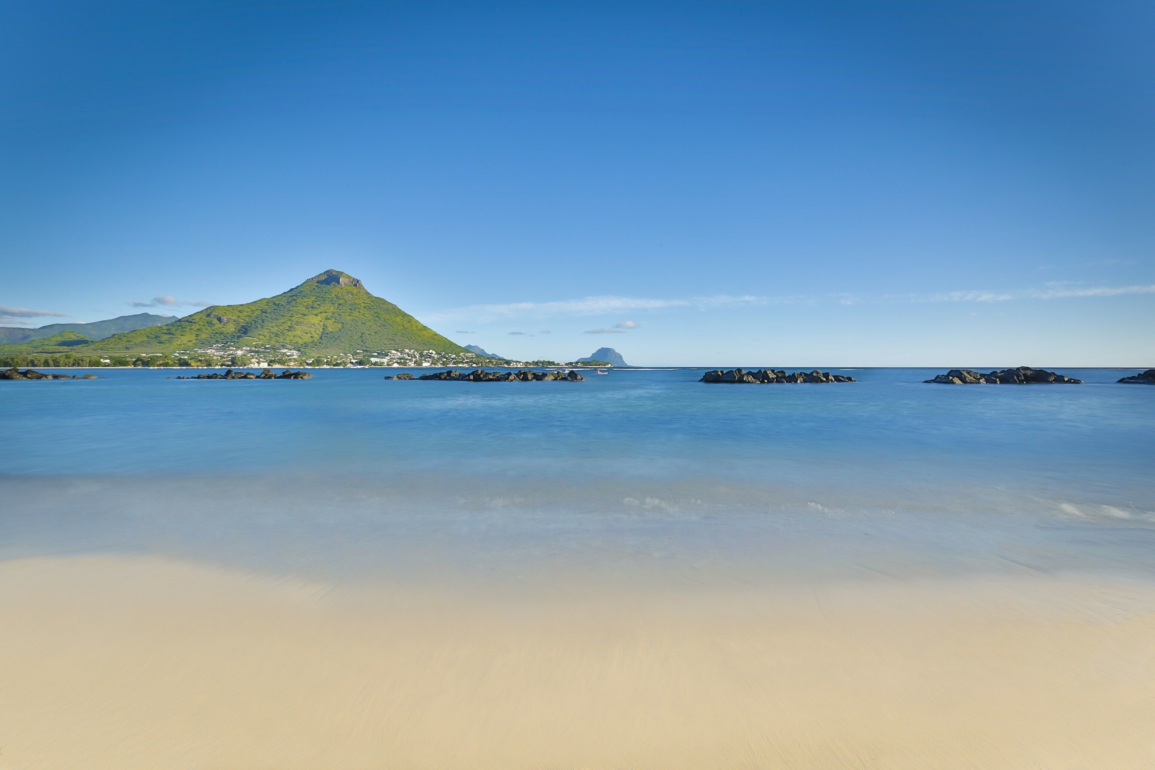 Una playa con agua cristalina, una montaña y algunas rocas.