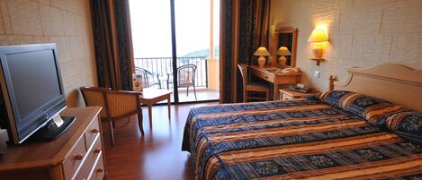 Habitación de hotel con cama, escritorio, silla, televisor y balcón con vistas.