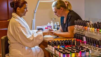 Un salón de belleza donde una mujer se está haciendo la manicura, con una lámpara y varios frascos de esmalte en la encimera.