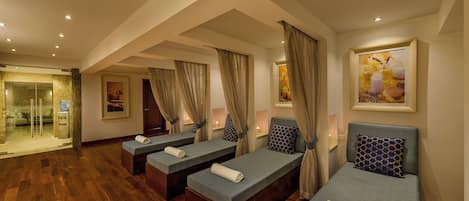 A spa room with three massage tables, wooden flooring, and a glass door leading to a bathroom.