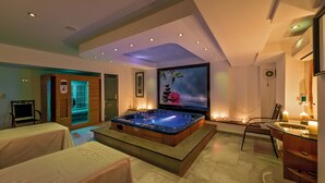 Un spa moderno con un jacuzzi, mesas de masaje y una pantalla grande que muestra una escena natural.
