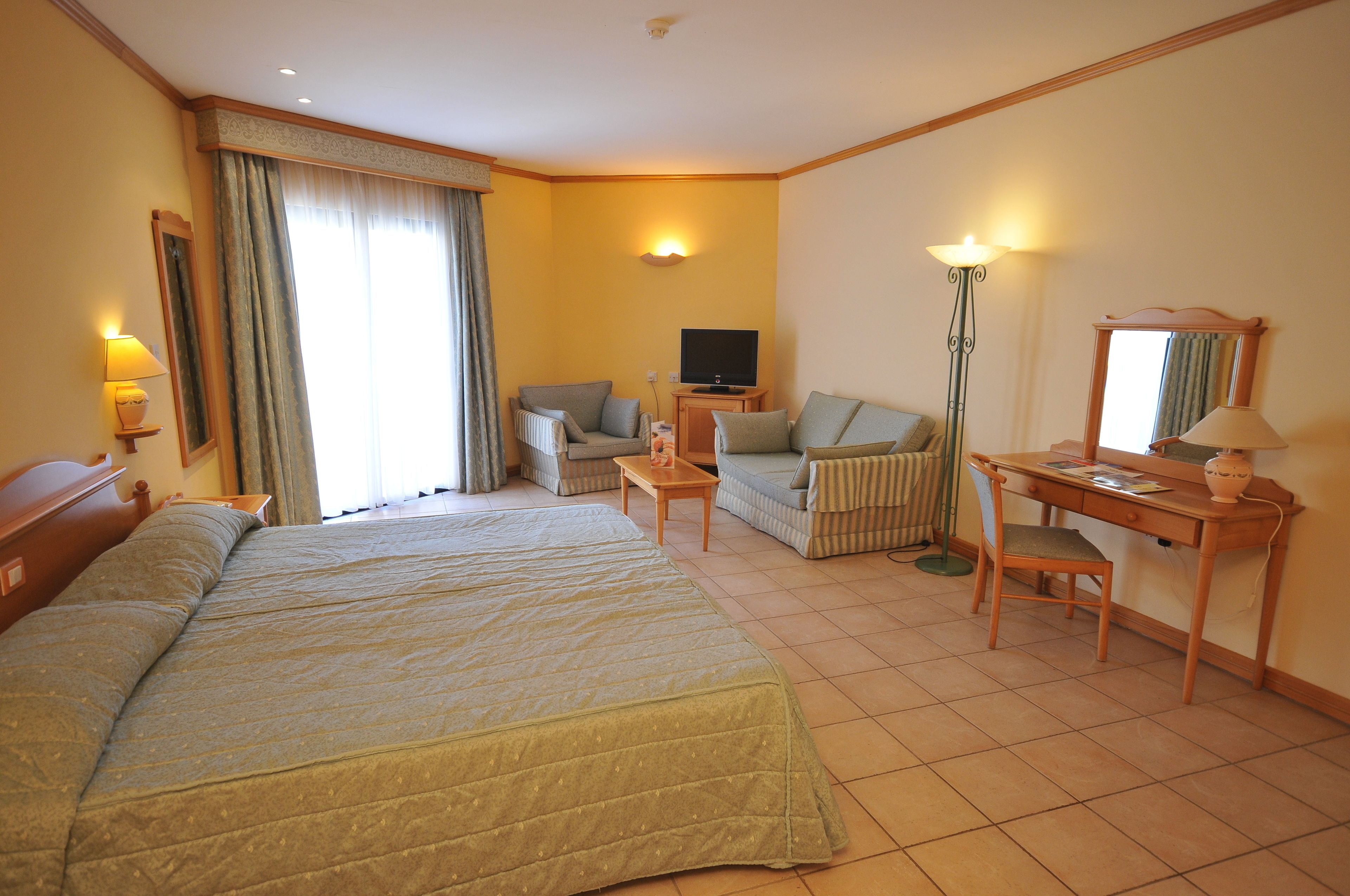 A hotel room with a large bed, a desk, a chair, a television, and a lamp.