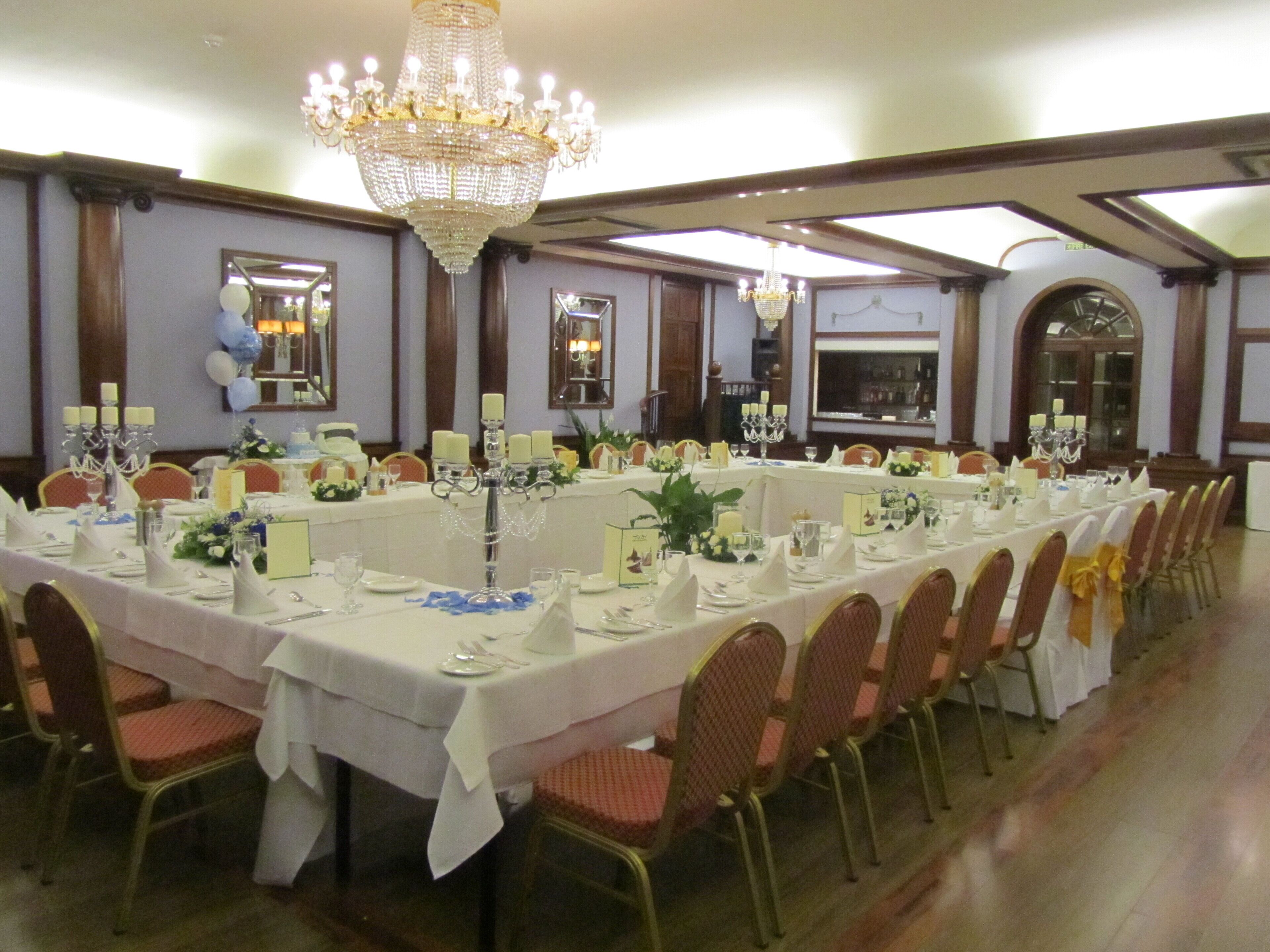 A banquet hall with long tables set for a formal event, chandeliers, and classic architecture.
