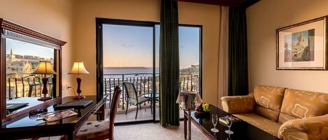 A hotel room with a balcony, a dining area, a sofa, and a table with a wine glass.