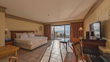 Habitación de hotel con cama, escritorio, silla, televisión y balcón con vistas.