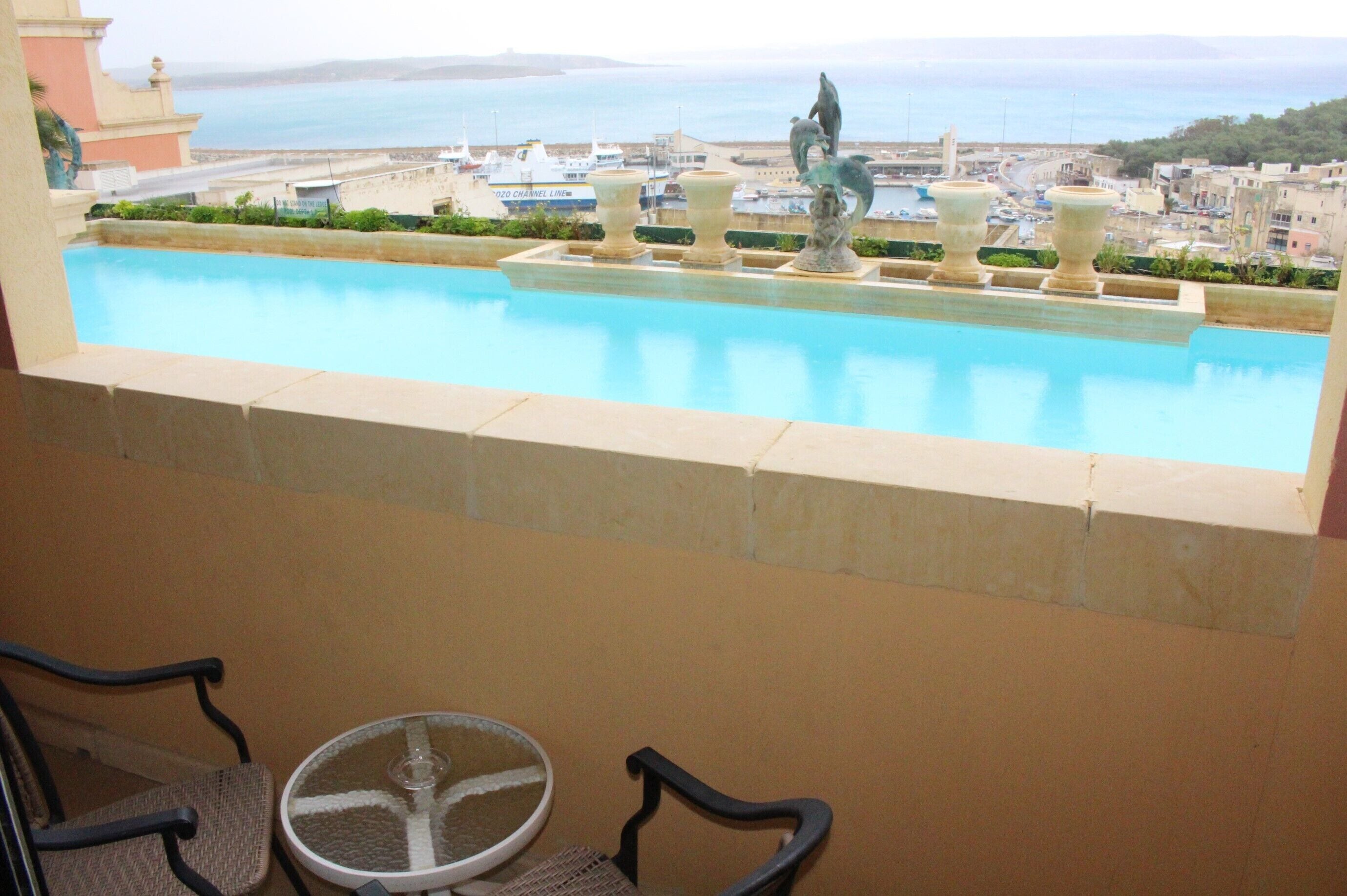 Ein Pool mit dekorativen Urnen und einer Statue mit Blick auf einen Hafen und eine Küstenstadt.
