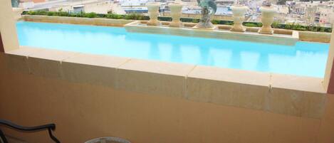 A pool with decorative urns and a statue, overlooking a marina and coastal town.
