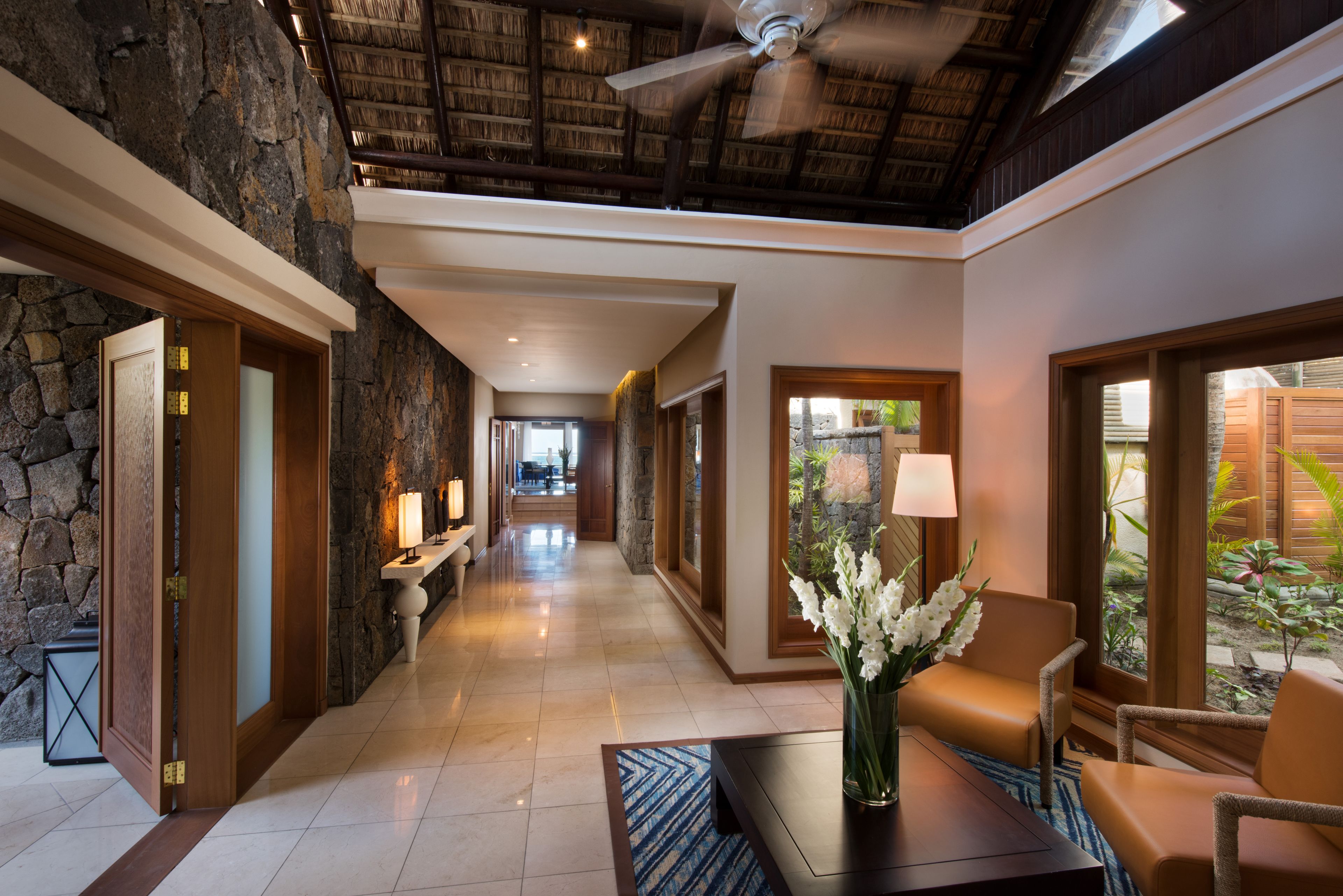 A hotel lobby with a stone wall, a ceiling fan, a reception desk, and a seating area with a table and chairs.