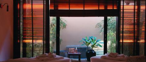 Un cuarto de spa con dos camillas de masaje, una mesita con artículos de tocador y vista a un jardín a través de una puerta corredera.